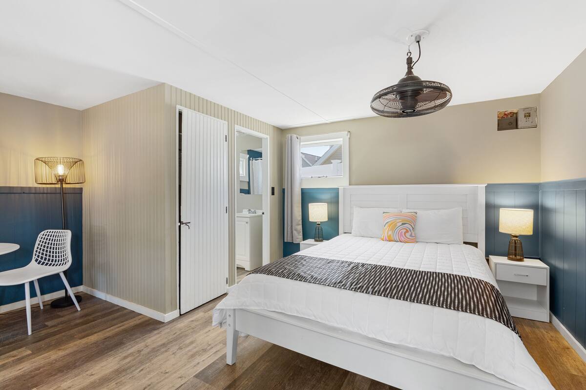 A hotel room with a bed, bedside tables, a chair, a desk, and a window.