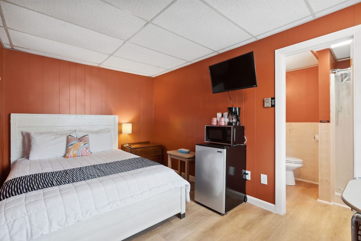 A hotel room with a large bed, a flat-screen TV mounted on the wall, a small refrigerator, a microwave, and a bathroom visible through an open door.