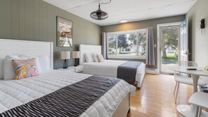 A hotel room with two beds, a desk, a chair, a window with curtains, and a ceiling fan.