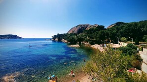 A coastal beach scene with clear water, rocky outcrops, and lush greenery.