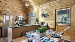 A cozy cabin interior with wooden walls, a kitchen with modern appliances, a dining area set for four, and a 'Home Sweet Home' sign. - Award winner| Dollywood |Arcades|Hot tub |GSMNP (Sevierville)