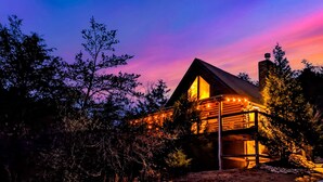 A log cabin with a large window and a chimney, surrounded by trees. - Award winner| Dollywood |Arcades|Hot tub |GSMNP (Sevierville)