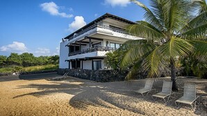 Ein zweistöckiges Anwesen am Strand mit Balkon, Steinmauer und Palmenbaum.