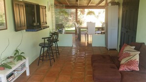 A cozy living area with a brown sofa, a white coffee table, and a tiled floor. There is a kitchen area with a dining table and chairs visible in the background. - Adorable 1-bedroom Pet-friendly Studio (Cayey, PR)