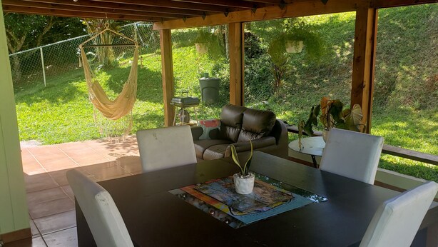 An outdoor patio with a table, chairs, a hammock, and a view of a lush garden. - Adorable 1-bedroom Pet-friendly Studio (Cayey, PR)