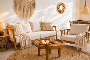 Un salon chaleureux avec un canapé, des fauteuils, une table basse ornée de bougies, une lampe et des éléments décoratifs accrochés au mur.