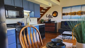 Una cocina moderna con armarios azules, una silla de madera, un letrero de cafetería y un comedor con una mesa dispuesta para dos personas.