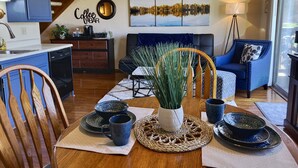 Una sala de estar acogedora con una mesa de comedor para dos, una barra de café y una vista panorámica de un lago.