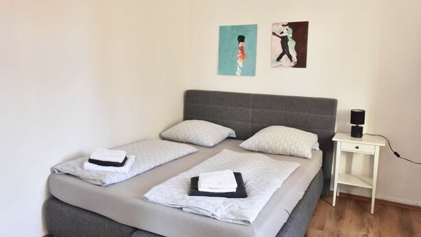 A double bed with two pillows, a bedside table with a lamp, and two wall art pieces.