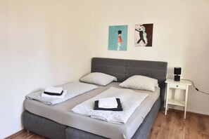 Un lit double avec deux oreillers, une table de chevet avec une lampe et deux œuvres d’art murales.