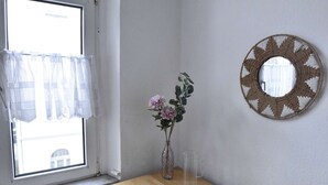 Une pièce avec une table en bois, un vase rempli de fleurs, une carafe en verre transparent et un miroir tissé accroché au mur.