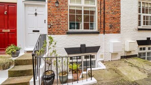 A brick house with a white door, numbered 2, and a small balcony with potted plants.