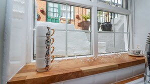 A kitchen with a wooden countertop, a white refrigerator, and a window with a view of a brick building and greenery outside.