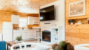 Un intérieur de chalet chaleureux avec une cheminée, des murs en bois, un téléviseur à écran plat et un coin repas.