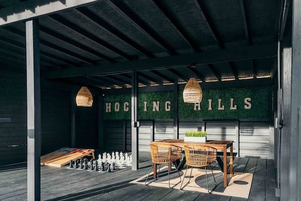 An outdoor seating area with a chessboard, wooden chairs, and a wall with 'HOGGING HILLS' text.