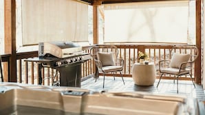 Un bain à remous, un barbecue et des fauteuils en osier sur une terrasse en bois.