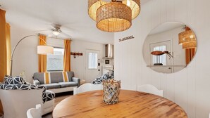 A cozy living room with a round wooden table, a sofa with patterned cushions, a floor lamp, and a large mirror on the wall. - 5041 The Captains Quarters *1 Block to Boat Access (Kill Devil Hills)