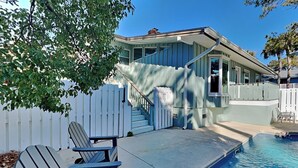 A pool area with a blue chair, a white picket fence, and a house with a porch.
