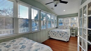 A bedroom with two beds, a ceiling fan, and large windows with blinds.