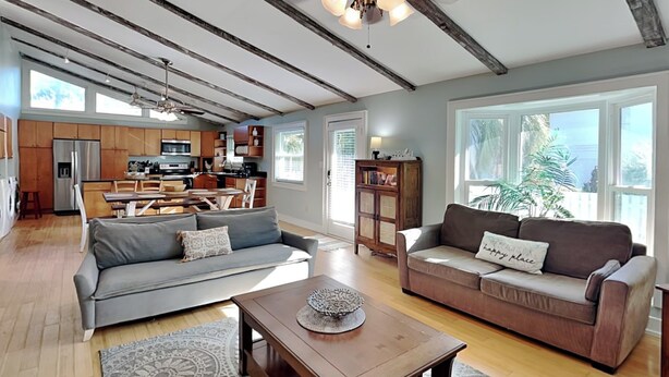 A spacious living room with a gray sofa, a brown sofa, and a wooden coffee table. There is a kitchen in the background with wooden cabinets and a refrigerator.