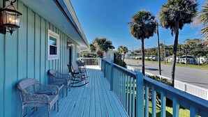 A porch with rocking chairs and a railing overlooking a street with palm trees.
