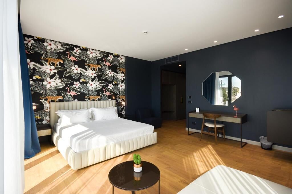 A modern hotel room with a large bed, a desk, a chair, and a mirror.