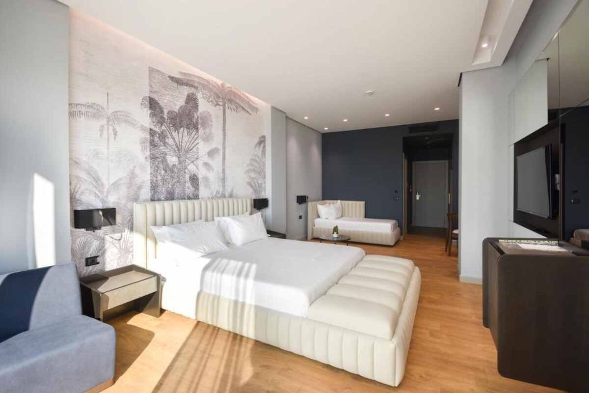Una camera da letto moderna con un letto grande, un divano, una TV e un'opera d'arte appesa al muro.