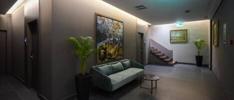 A modern lobby with a sofa, potted plants, a staircase, and artwork on the walls.
