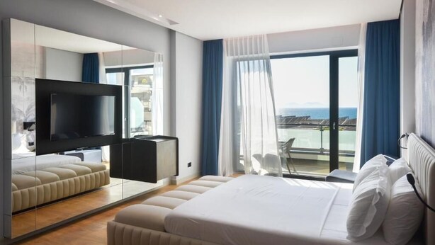 Ein modernes Hotelzimmer mit einem großen Bett, einem Flachbildfernseher, einer Sitzecke und einem Balkon mit Blick.