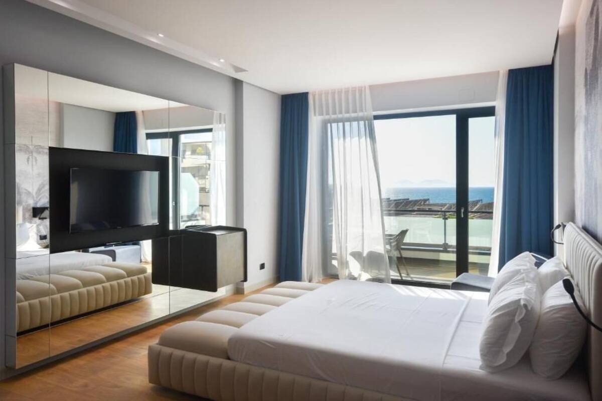 Una camera d'albergo moderna con un letto grande, una TV a schermo piatto, un'area salotto e un balcone con vista.