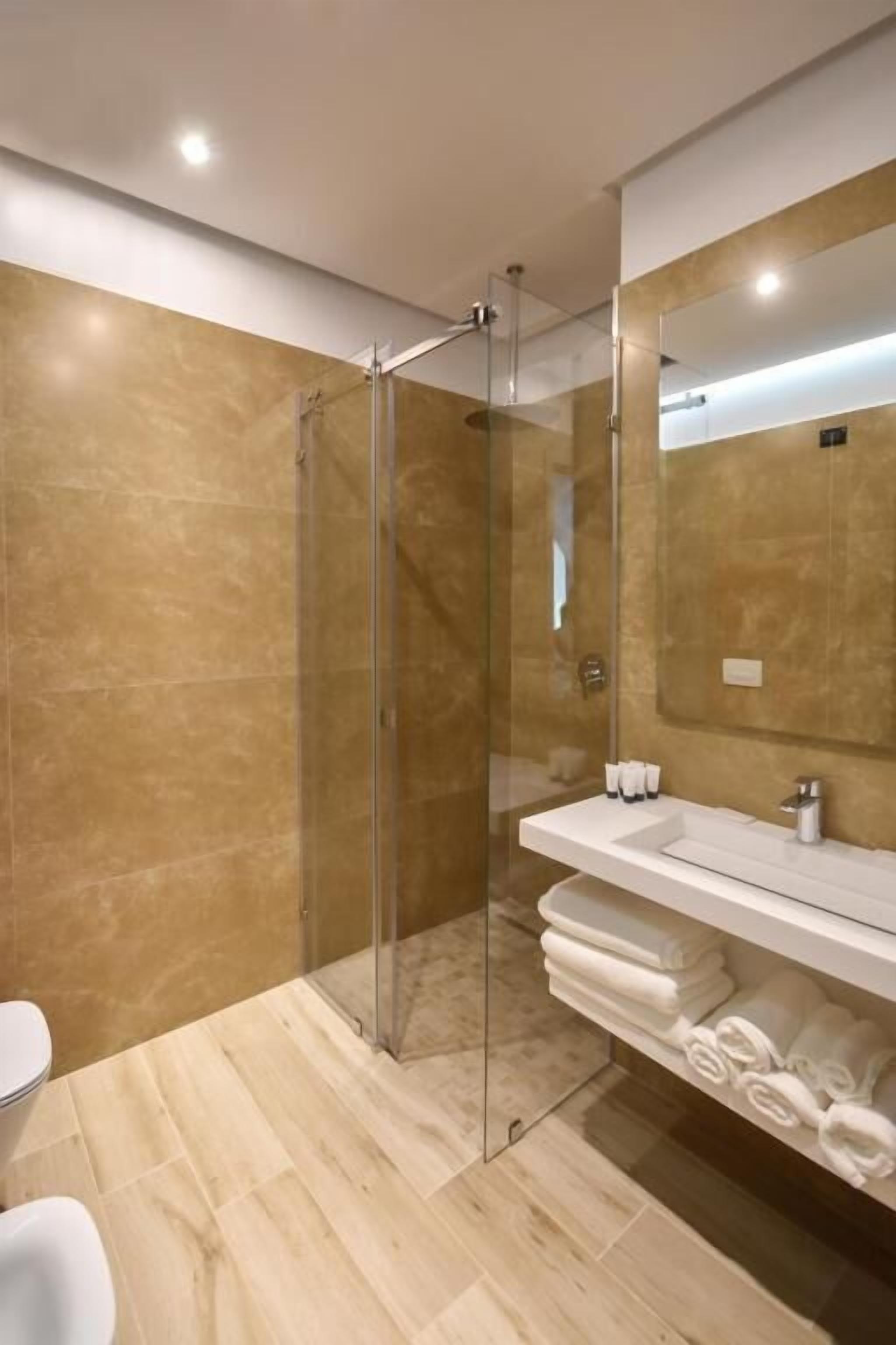 Un baño moderno con ducha envuelta en vidrio, un lavabo blanco y un espejo encima.