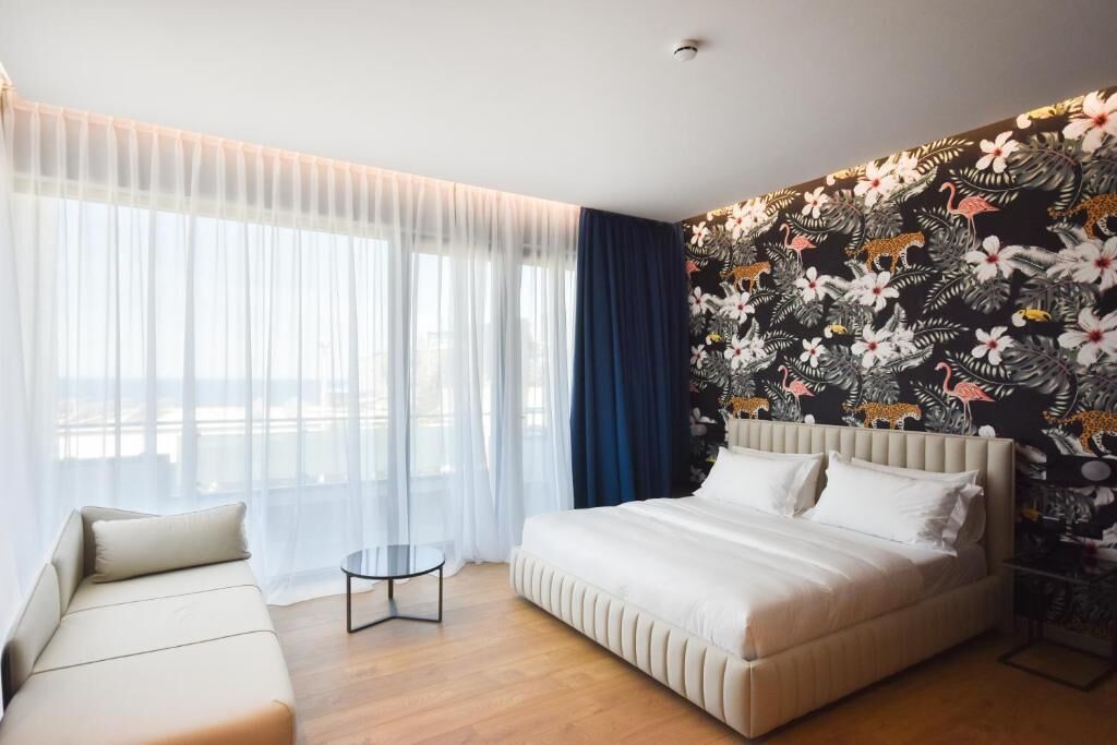 Een moderne hotelkamer met een groot bed, een slaapbank, een klein rond tafeltje en een wand met een bloemenmotief.