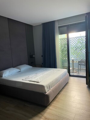 Un dormitorio con cama, mesita de noche, ventana con cortinas y vistas a un espacio exterior.