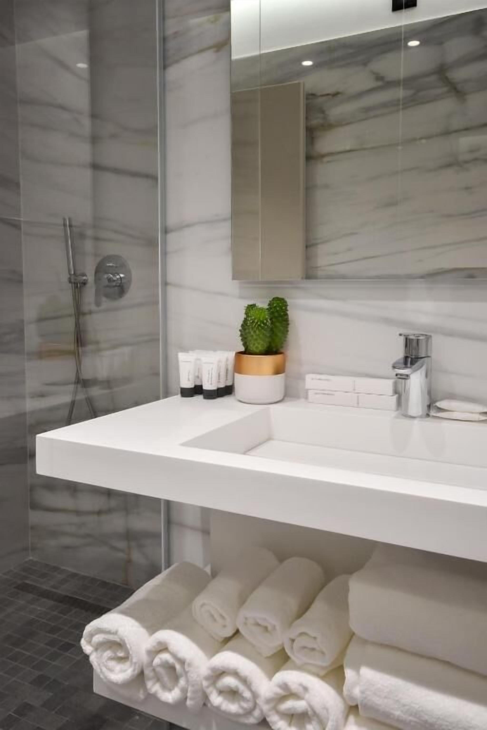 Un baño moderno con lavamanos de mármol, cabina de ducha de vidrio y toallas dobladas con cuidado.