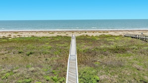 Ein hölzerner Steg führt zu einem Strand bei blauem Himmel.