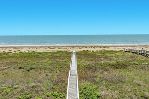 Een houten looppad dat naar een strand leidt, onder heldere lucht.