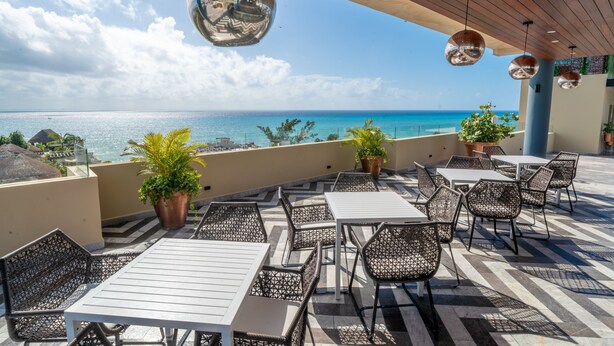 A terrace with outdoor seating, potted plants, and a view of the ocean. - Condo Jade - Singular Joy Residences (Playa del Carmen)