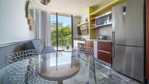 A modern kitchen with a glass dining table, stainless steel appliances, and a view of the outdoors. - Condo Jade - Singular Joy Residences (Playa del Carmen)