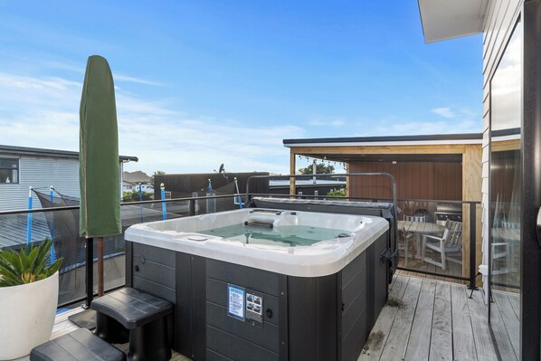 A hot tub on a wooden deck with a glass railing, a wooden pergola, and a view of a house in the background. - Tuturu Bliss - Ruakākā Holiday Home (Ruakaka)