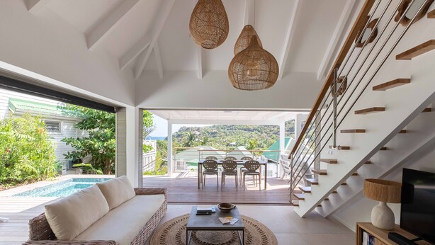 Ein modernes Wohnzimmer mit Sofa, Couchtisch und Fernseher, mit Blick auf einen Pool und einen Außenbereich zum Essen.
