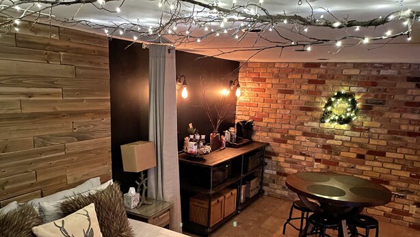 Una habitación acogedora con una pared de madera, una pared de ladrillo adornada con un adorno, una mesa de comedor con taburetes y un sofá con cojines decorativos.