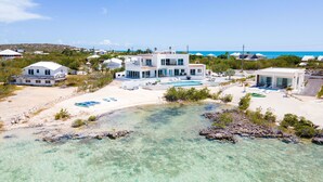Une propriété située en bord de mer, comprenant plusieurs maisons modernes, une piscine et une eau turquoise cristalline.