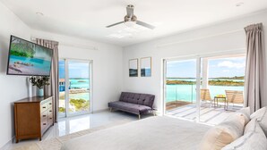 Une chambre avec un grand lit, un canapé, une télévision et un balcon offrant une vue sur la mer.
