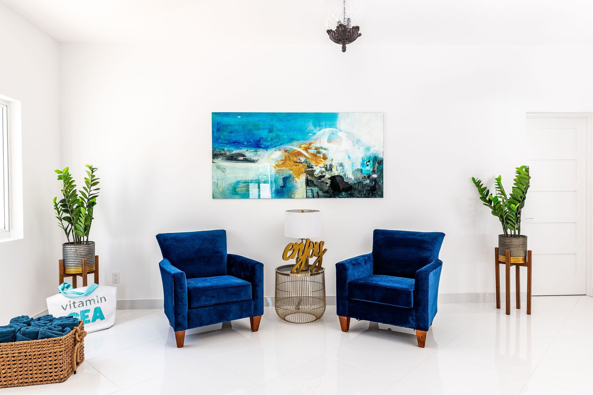 Een moderne woonkamer met twee blauwe fluweelzitzakken, een groot abstract schilderij en potplanten.