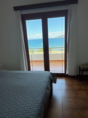 Een kamer met een bed, uitzicht op zee door een schuifdeur en een betegelde vloer.