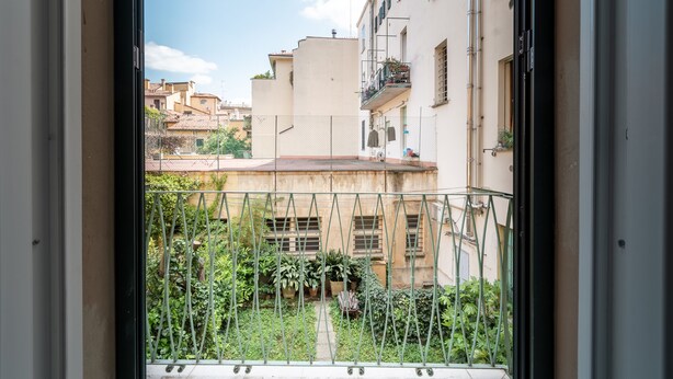 A view through a window with a metal railing, overlooking a courtyard with potted plants and buildings in the background. - HouSmart San Carlo 17 (Bologna)