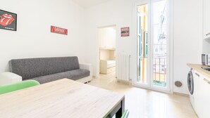 A modern living room with a grey sofa, a wooden table, and a kitchen area with a washing machine. - HouSmart San Carlo 17 (Bologna)