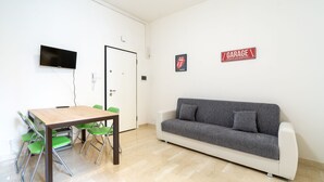 A room with a wooden table, green chairs, a grey sofa, a TV mounted on the wall, and a door with a 'Garage' sign. - HouSmart San Carlo 17 (Bologna)