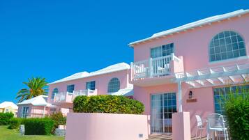 A pink building with multiple balconies, large windows, and a patio area with chairs.