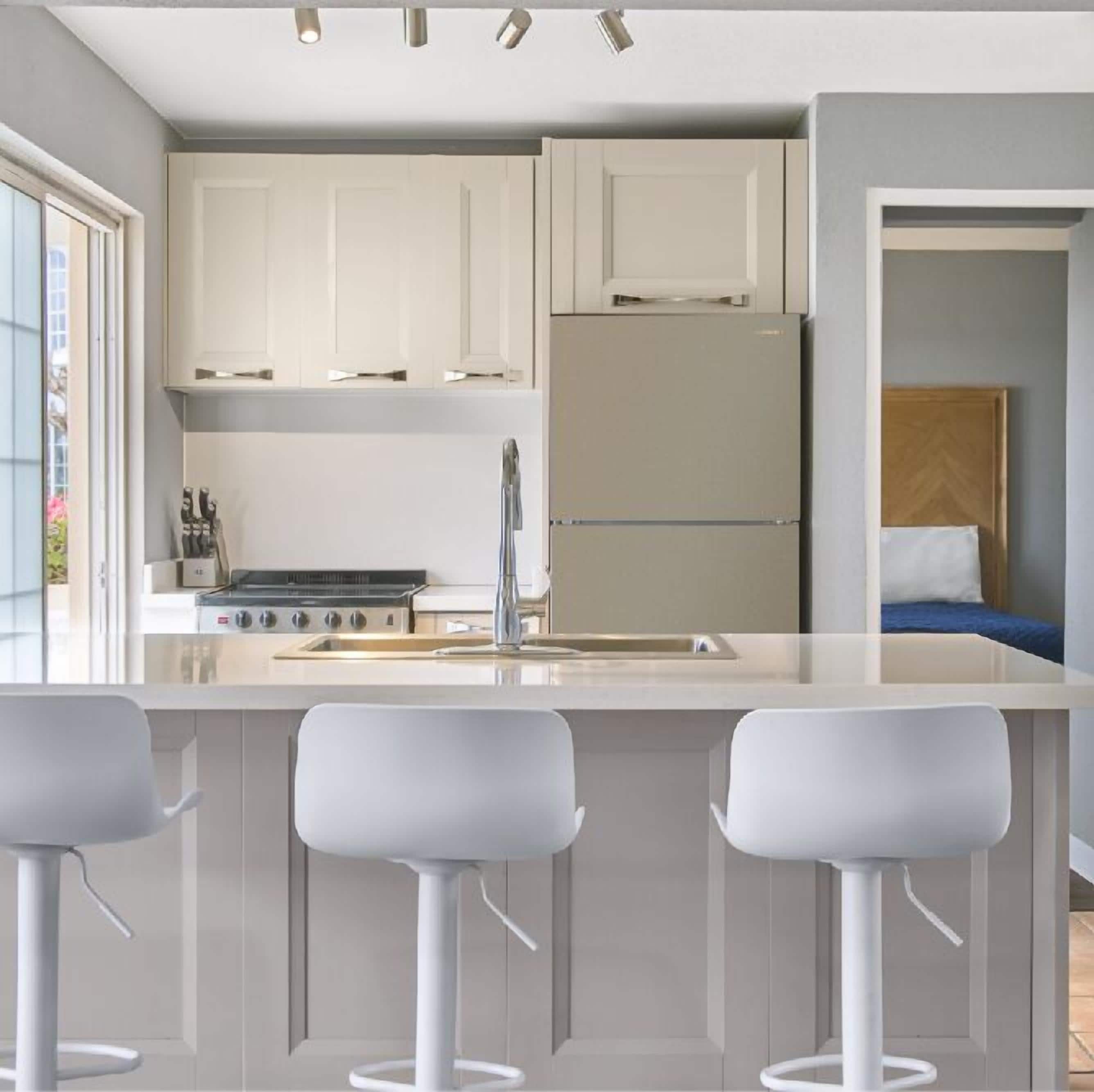 Una cocina moderna con armarios blancos, una isla central con taburetes de bar y un horno empotrado.